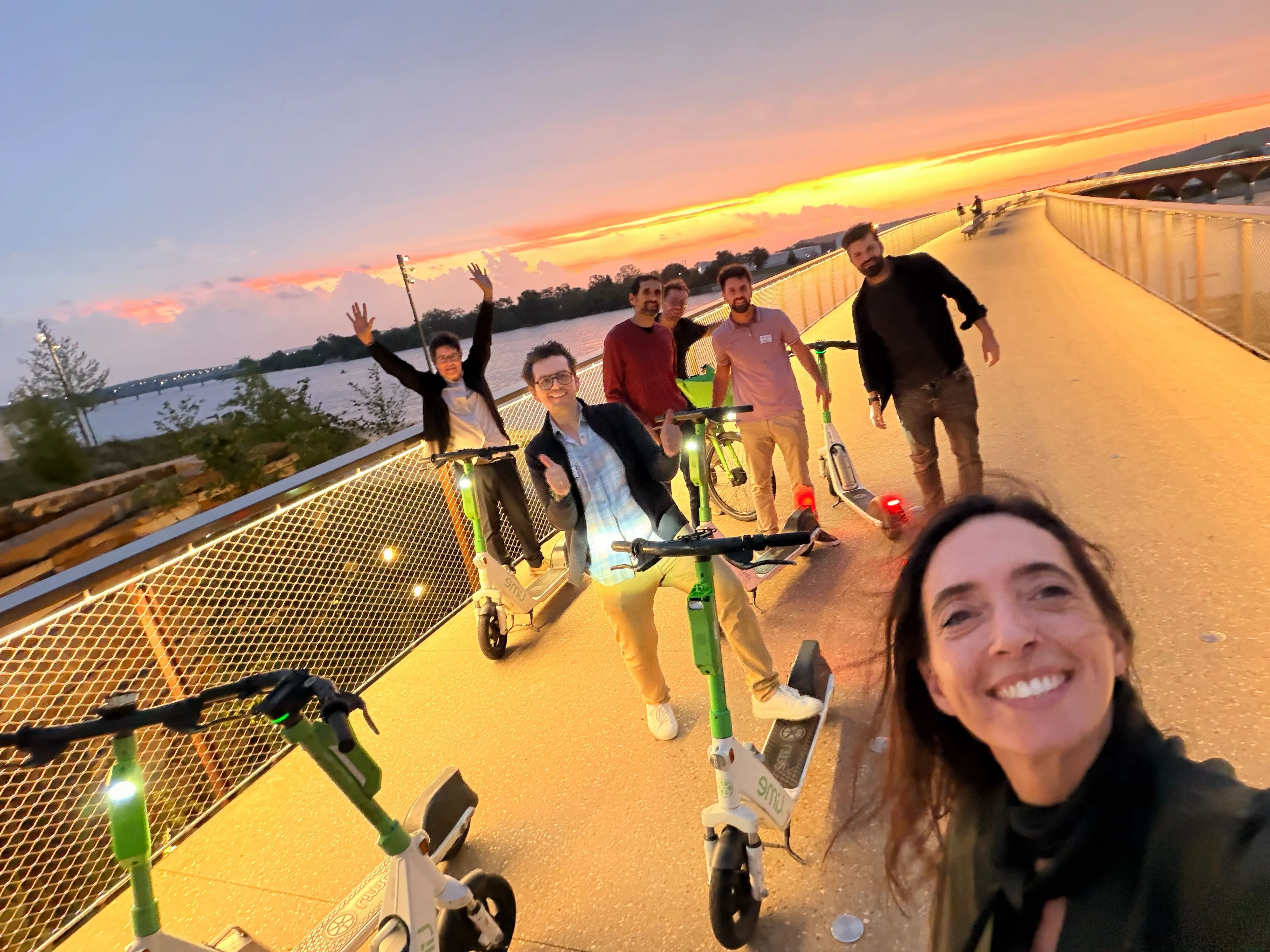 Team riding scooters along the river at sunset